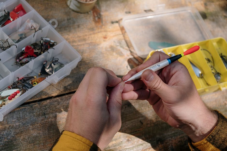 Close-up of hands organizing fishing gear with lure box on a wooden surface.
