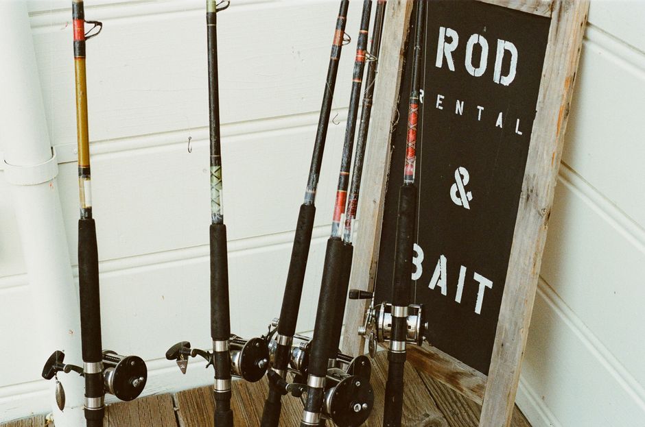 Collection of fishing rods beside a bait rental sign outdoors.